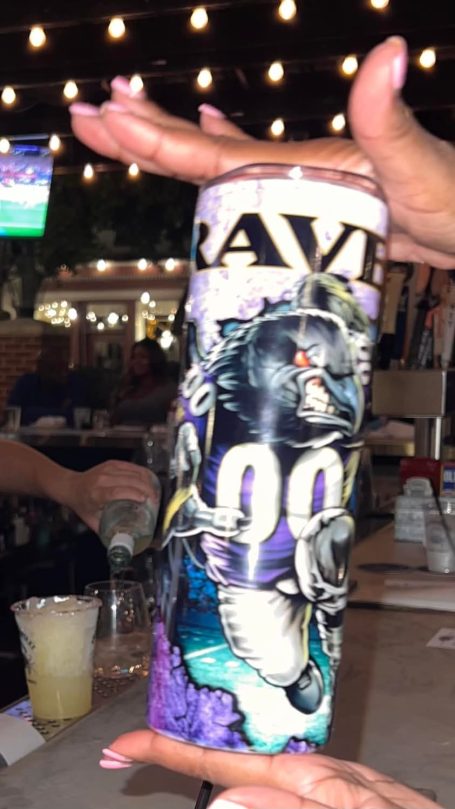 A person holding a decorative Ravens-themed cup with a football design.