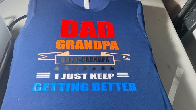 Blue t-shirt with the words "DAD GRANDPA" and "I just keep getting better" in bold colors.