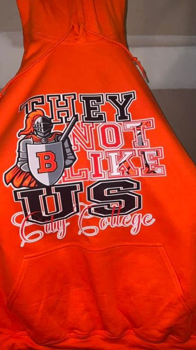 Bright orange hoodie with "They Don't Like Us" and "B" graphic design.